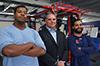 Hurricane football team head coach stands in the middle of two of his players who are team captains in the weight room.