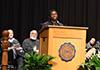 George Lahai stands at the podium while people sit and listen to his speech.