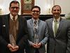 Four men standing side by side smiling. The two men in the middle are holding alumni awards. 